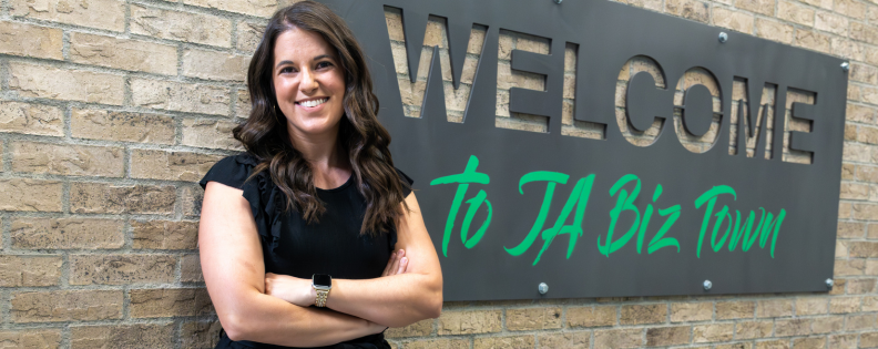 Woman standing front of a sign that says "welcome to JA biz town" at the Junior Achievement of Arizona