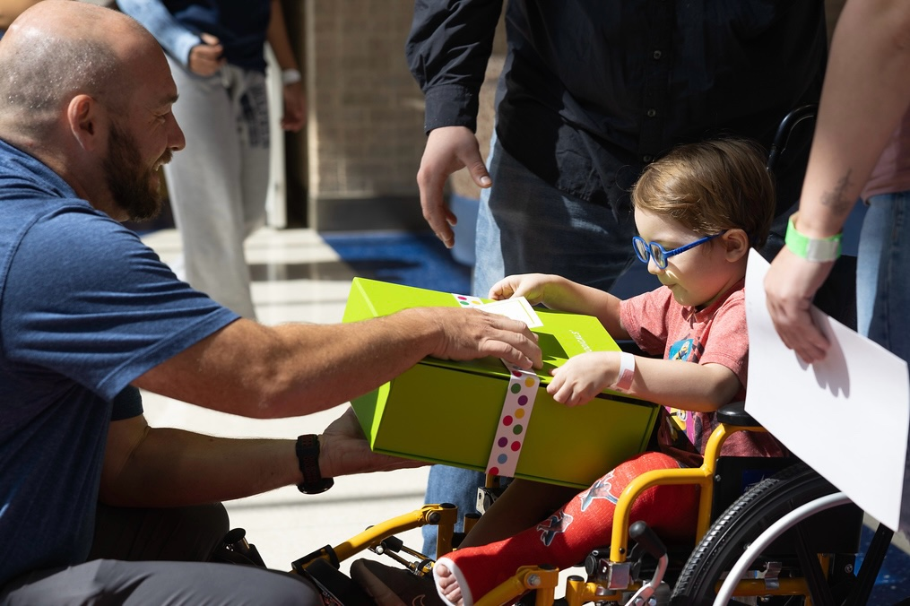 Cheeriodicals care packages, man hands present to child in wheelchair 