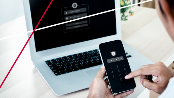 person entering a two-factor authentication code on a mobile phone in front of a laptop to protect against ai fraud