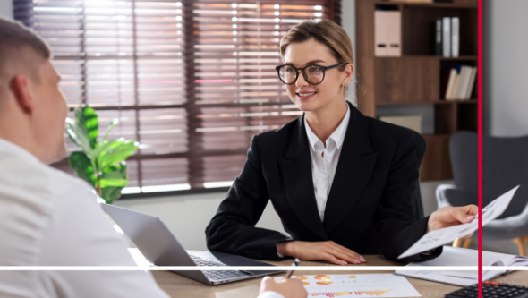 Man and Woman sitting at a desk speaking to each other.