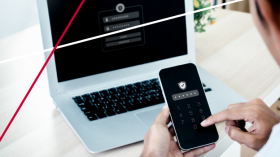 person entering a two-factor authentication code on a mobile phone in front of a laptop to protect against ai fraud