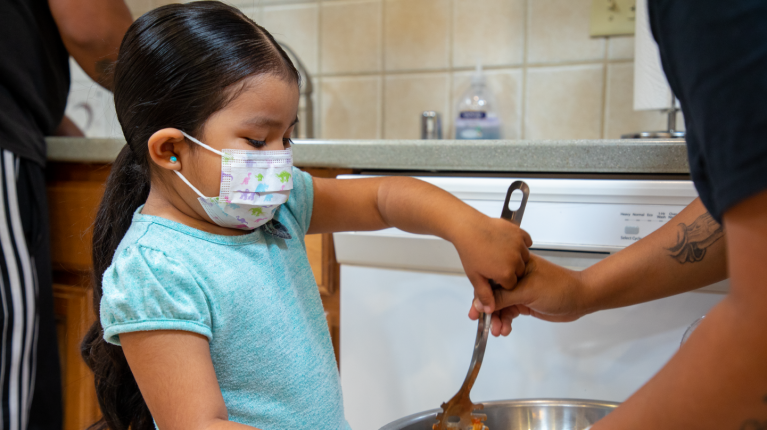 child with mask on while cooking food